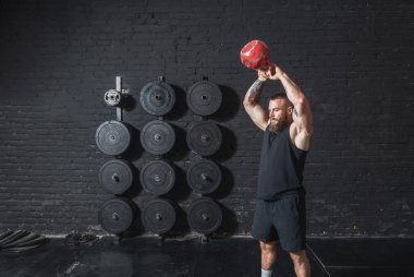Genç, terli, kaslı, formda, iri kaslı bir adam spor salonunda kettlebell salıncak egzersizi yapıyor.