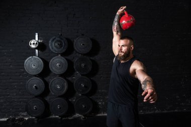 Genç, terli, güçlü, kaslı, iri kaslı bir adam. Spor salonunda kettlebell kapma egzersizi yapıyor.