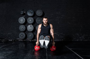 Genç, terli, formda, iri kaslı, kaslı, kaslı bir adam. Vücut kaslarını çalıştırıyor. Spor salonundaki iki su ısıtıcısının üstünde bacakları var. 