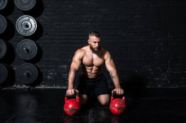 Genç, terli, formda, güçlü, kaslı bir adam. Sert Kettlebell antrenmanından sonra spor salonunda mola veriyor.