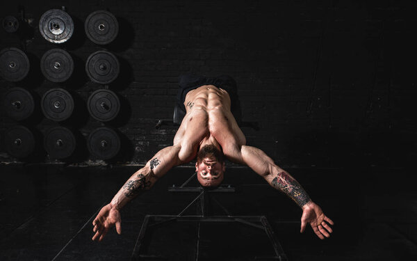 Молодой потный сильный мускулистый мужчина с большими мышцами делает упражнения на прессе на скамейке в тренажерном зале, как хардкор кросс обучение реальных людей