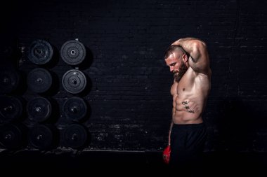Genç, terli, güçlü, kaslı, kaslı, spor salonunda karın kası egzersizi yapan, tek eliyle ağır bir kettlebell çeken bir adam.