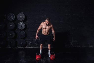 Genç, terli, güçlü, kaslı bir adam. Büyük kasları var. Kettlebell antrenmanına hazırlanıyor ve konsantre oluyor.