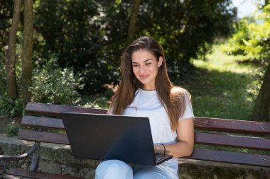 Genç serbest çalışan bir kadın ya da kız parkta oturmuş internet üzerinden erkek arkadaşı ya da iş arkadaşıyla sohbet ediyor.