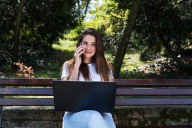 Genç serbest çalışan kadın ya da kız parktaki bankta oturmuş iş ve yeni proje hakkında iş arkadaşı ile akıllı telefonuyla konuşuyor.