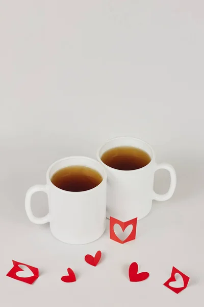 Red paper hearts and two white cups on white background with copy space. Valentine\'s day, love, couple, wedding concept