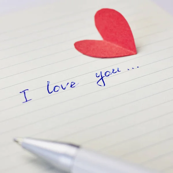 Paper page of notepad with sign I love you, pen and red paper heart. Valentine\'s day, wedding, love concept
