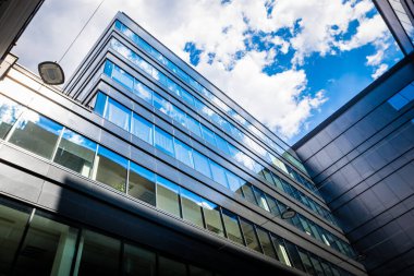 Modern mimarinin dış kısmının bir parçası. Alışveriş merkezi. İş merkezi. Beyaz bulutlu mavi gökyüzünün arka planında mat siyah duvarlarda kare pencereler.