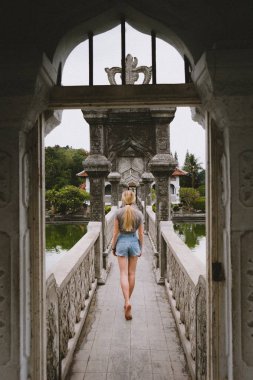 Sarışın kız çekip tarihsel Bali hindu tapınağı, su ile çevrili bir taş köprü