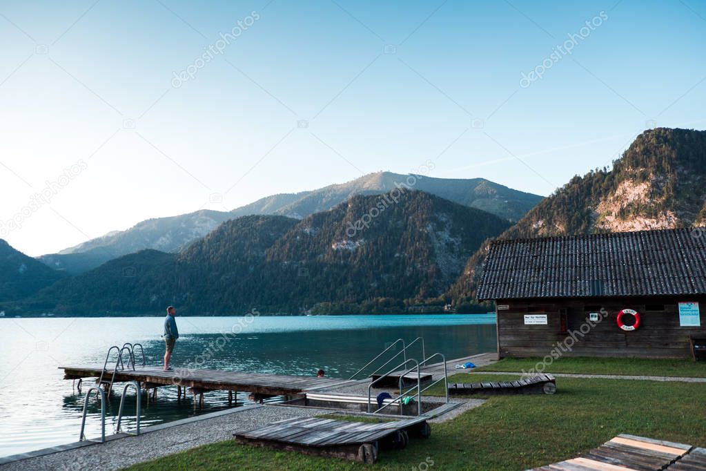 Young man standing at dock on lake and looking at mountains