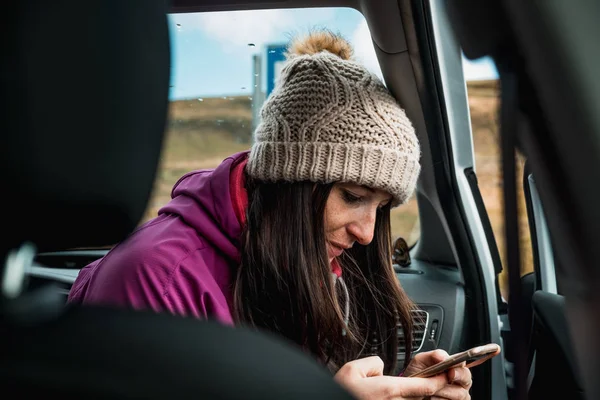 young woman in knitted hat using mobile phone sitting in car