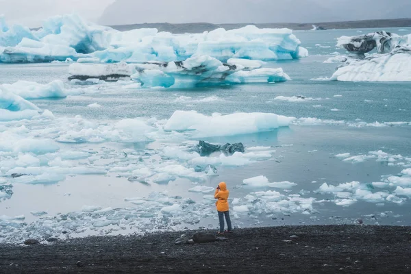 Young girl standing on the sea shore covered in ice floes looking at the Nordic landscape in Iceland