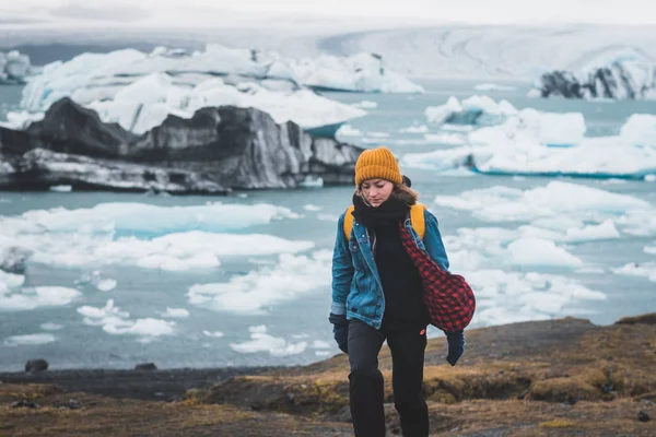 Young girl standing on the sea shore covered in ice floes looking at the Nordic landscape in Iceland