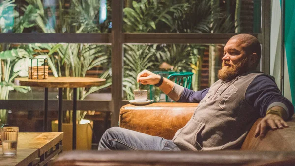 リラックスして 素敵なカフェや緑豊かな植生の多くのレストランでコーヒー カプチーノ ひげを持つ男 — ストック写真