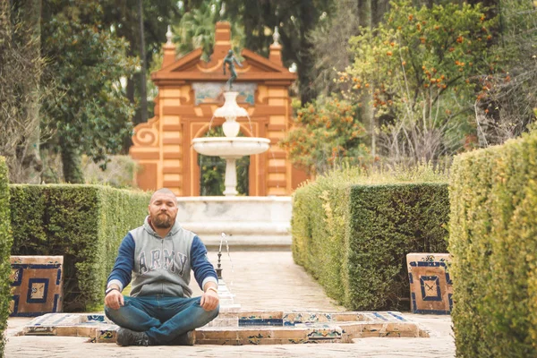 Bearded man sitting and relaxing by meditation in the garden of Real Alcazar de Sevilla