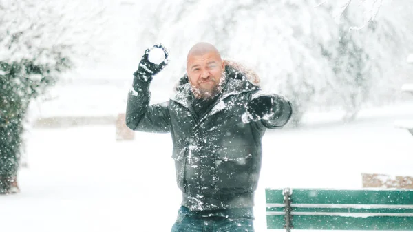 Man with beard and shaved head is ready to throw a snowball in a park or forest during a big snowfall - winter 2018 2019