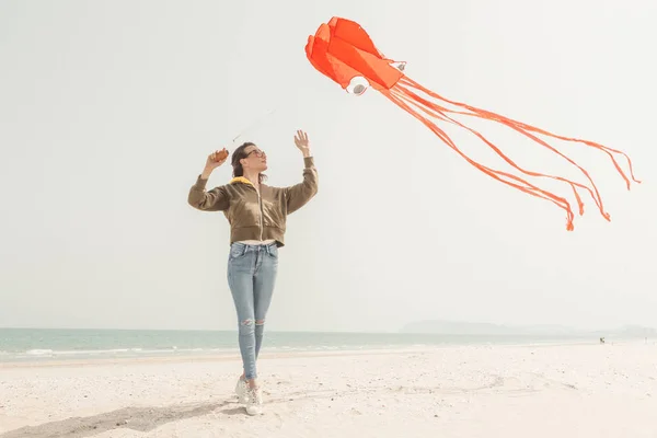 Young beautiful women launching a kite (red octopus) on the beach (seaside) during a sunny and foggy day