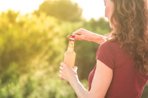 龍女が夕日に赤い シャツを着た立ってビールのボトルを開いてください — ストック写真