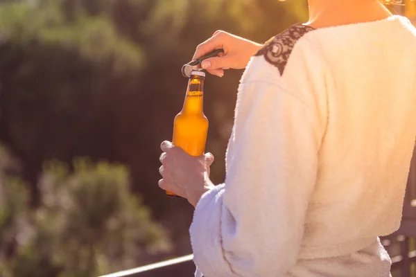 龍女は日没で白いバスローブで立ってビールのボトルを開く — ストック写真