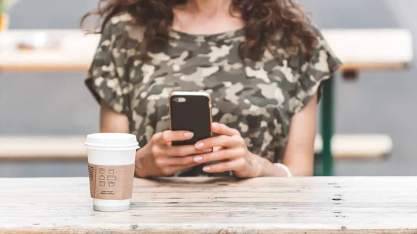 En ung kvinna ser smartphone med en kopp kaffe — Stockfoto