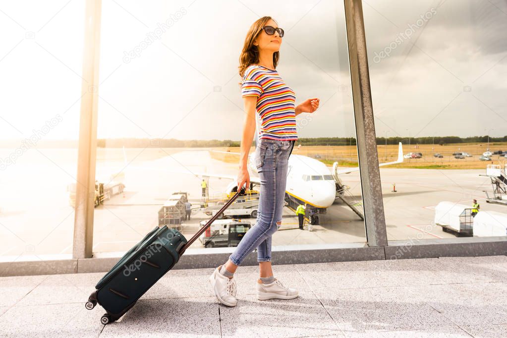 A young woman is waiting her flight in waiting hall in airport with her hand luggage
