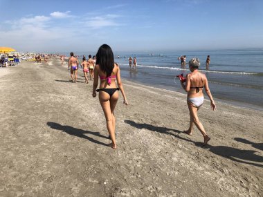 Riccione, Rimini / İtalya - 07 20 2018: genç ve yaşlı bir kadın arkadan görünüm (İtalya'da, Riccione), Adriyatik Denizi sahil boyunca yürüyor