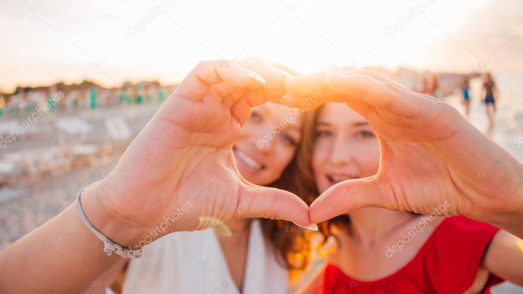 Two smiling girls (young women) making selfie photo on the beach with sunshine background.