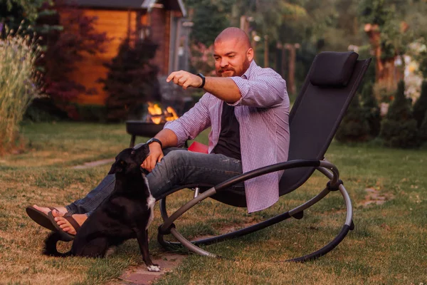 Young Man Sitting Rocking Chair Playing Little Black Dog Garden — Stock Photo, Image