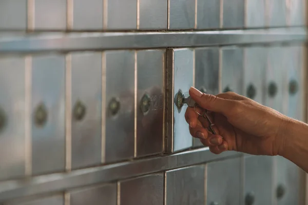 Close up of a female hand opening a mailbox with a small key - post office box or PO BOX concept - bank deposit box