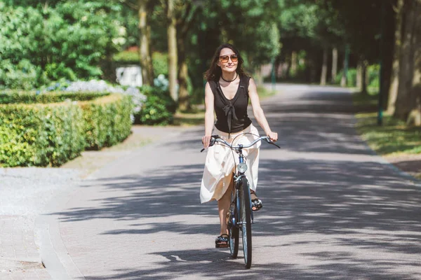 A young woman with romantic mood is cycling on her dutch bicycle on the countryside road in holland (Netherlands), wearing a vintage skirt - ecology and environmental sustainability concept