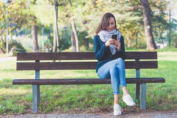 Millennial Girl Seduta Una Panchina Parco Guarda Suo Smartphone Con — Foto Stock