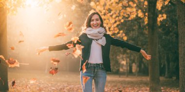 Kollarını açarak ve güneşli Sonbahar Doğa zemin üzerine sarı yapraklar ile gülümseyen güzel kadın