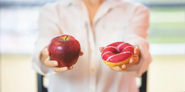 Womans hands holding red apple and a donut. Difficult choice, healthy raw food, sugar and fat addiction concept