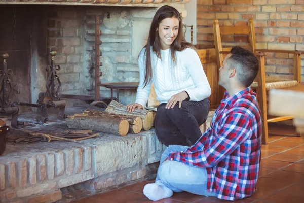 Young shy people (man and woman) met at friends party - young couple talking near the fireplace trying to kindle a fire - seduction and love, romantic date, winter holidays celebration concept