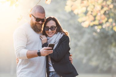 Romantik mutlu çifte randevuya eğleniyor. Bir şey onun kız arkadaşı smartphone üzerinde gösterilen büyük sakallı adam. Sonbahar güneşli gün batımı ruh hali.