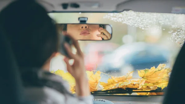 Young woman making kiss or duck face to rear-view mirror in a car. Shot from behind. Autumn mood.