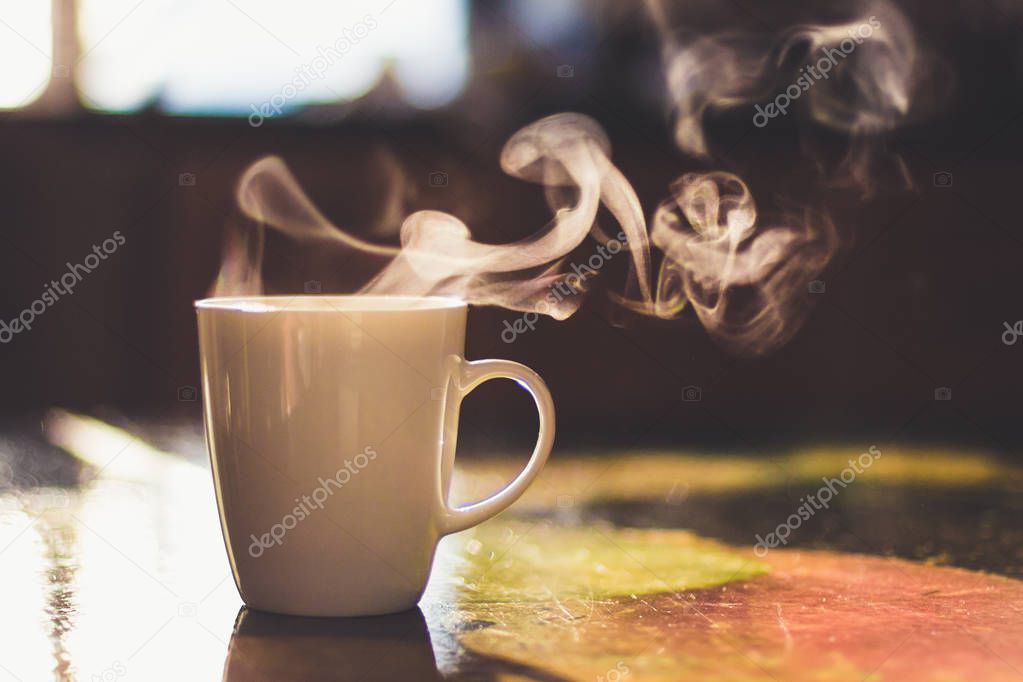 Close up of steaming cup of coffee or tea on vintage table - early morning breakfast on rustic background