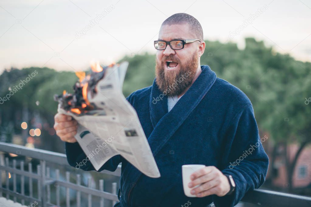 Portrait of excited (shocked) bearded man looking to the newspaper (on fire) - burning magazine in man's hands - hot and breaking news concept