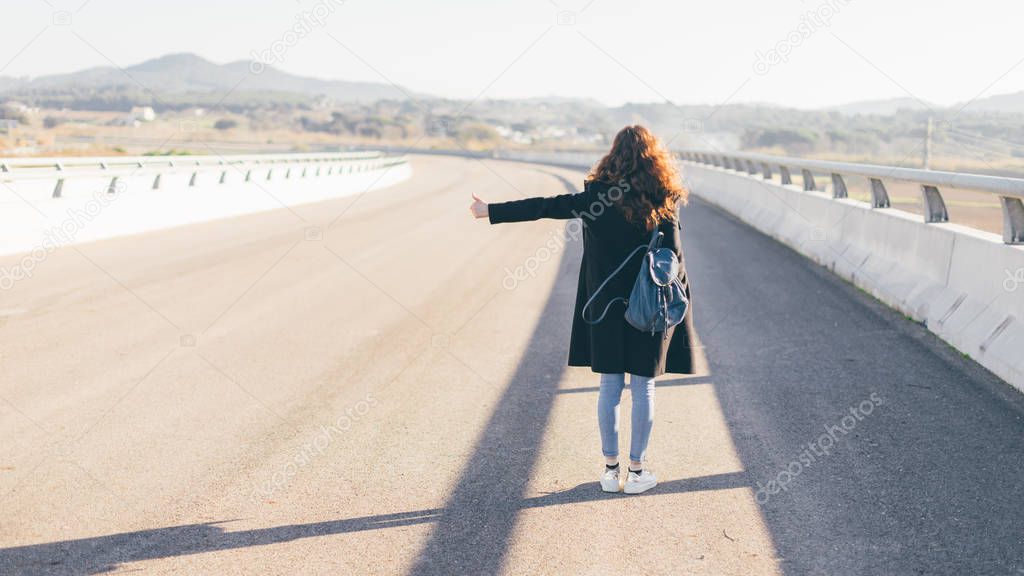 Girl try to stop a car on the road with thumb up - hitchhiking, autostop and traveling concept.