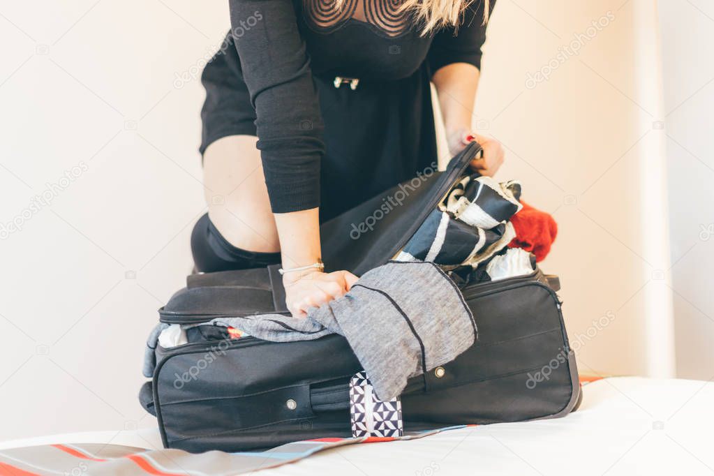 Woman trying to lock the suitcase on bed - luggage overweight and shopping concept.