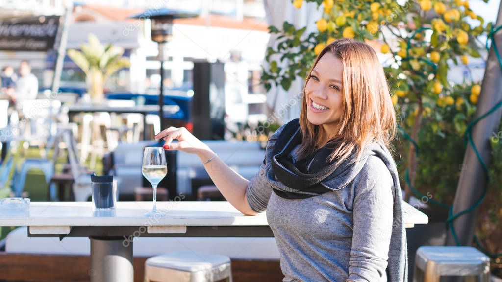Young beautiful smiling curvy woman sitting at restaurant with glass of white wine on a sunny day - food, beauty, spring concept