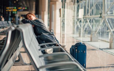 Young tired woman sleeping alone in empty airport with her hand luggage, waiting flight - transportation, low cost traveling, delayed or cancelled flight concept clipart