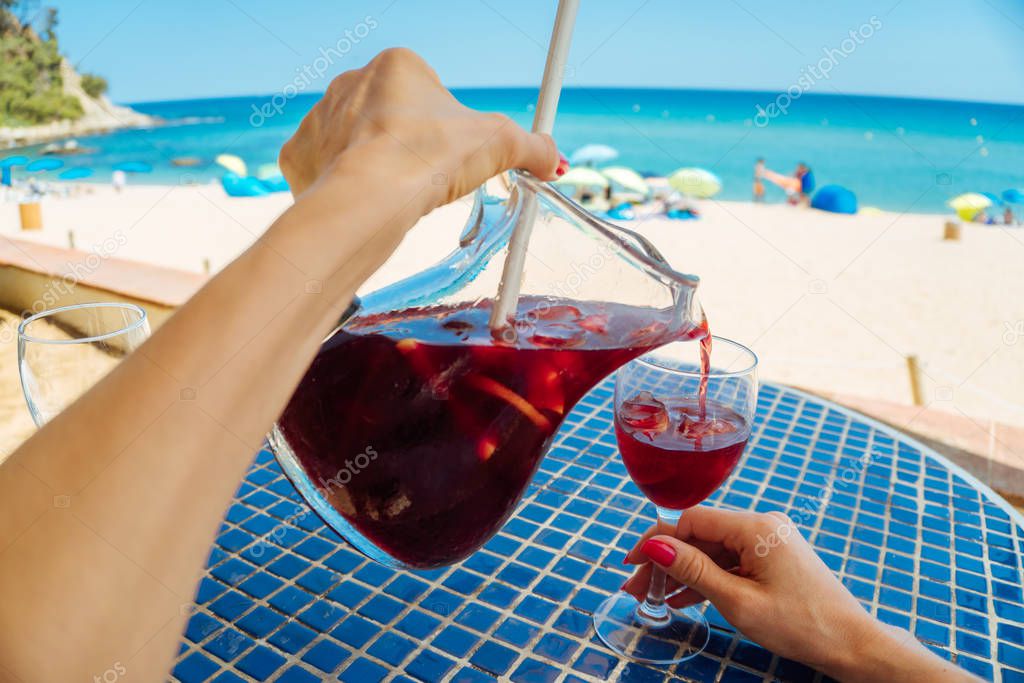 POV image of female hands pouring fresh red wine sangria into a glass - relax, vacation, leisure, freedom and good mood concept