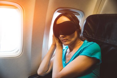 Young woman sleeping on a plane with black eye mask on her face - tired girl resting during a long flight - jet lag concept clipart