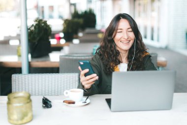 Mutlu asya gülümseyen bin yıllık kız dizüstü ekrana bakarak, elinde bir akıllı telefon tutarak - seyahat ederken bir kafede çalışan, dijital göçebe, film izlerken, görüntülü arama kavramı