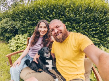 Mutlu, genç, gülümseyen bir çift köpekle birlikte parkta veya bahçede selfie çekiyor.