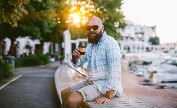 若いひげを生やした男がコーヒーを飲んで日の出に座っている肖像画 彼は再利用可能な竹の旅行マグカップを使用しています 持続可能なライフスタイルと観光の概念 — ストック写真