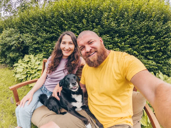 Mutlu, genç, gülümseyen bir çift köpekle birlikte parkta veya bahçede selfie çekiyor.