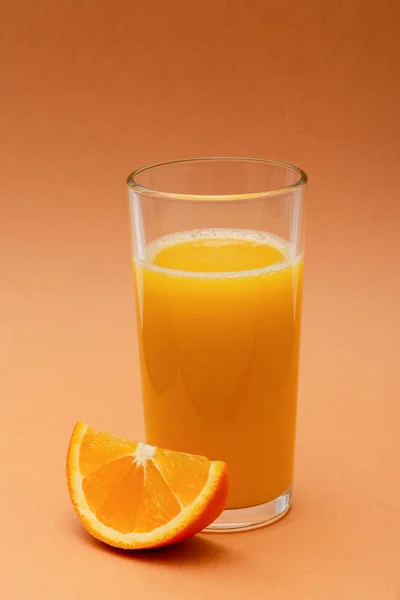 オレンジ色の背景にオレンジのスライスがあるオレンジジュースのグラス — ストック写真