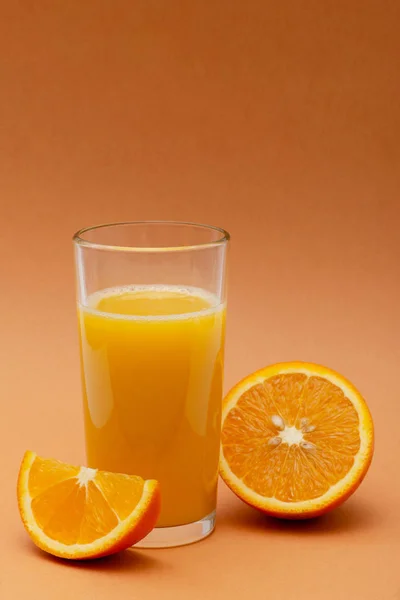 オレンジ色の背景にオレンジのスライスがあるオレンジジュースのグラス — ストック写真